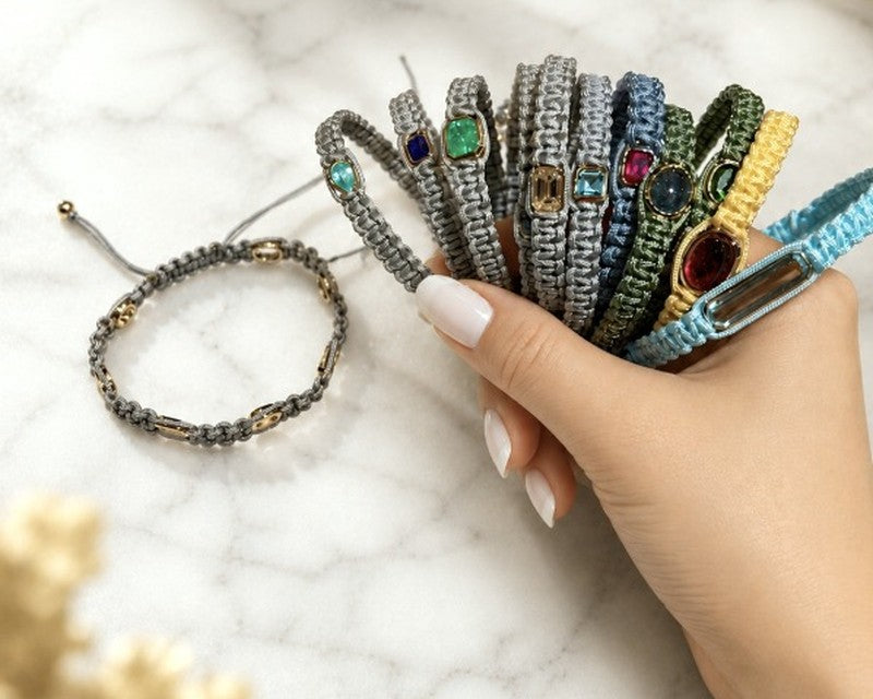 A hand holding a stack of woven cord bracelets set with colored gemstones