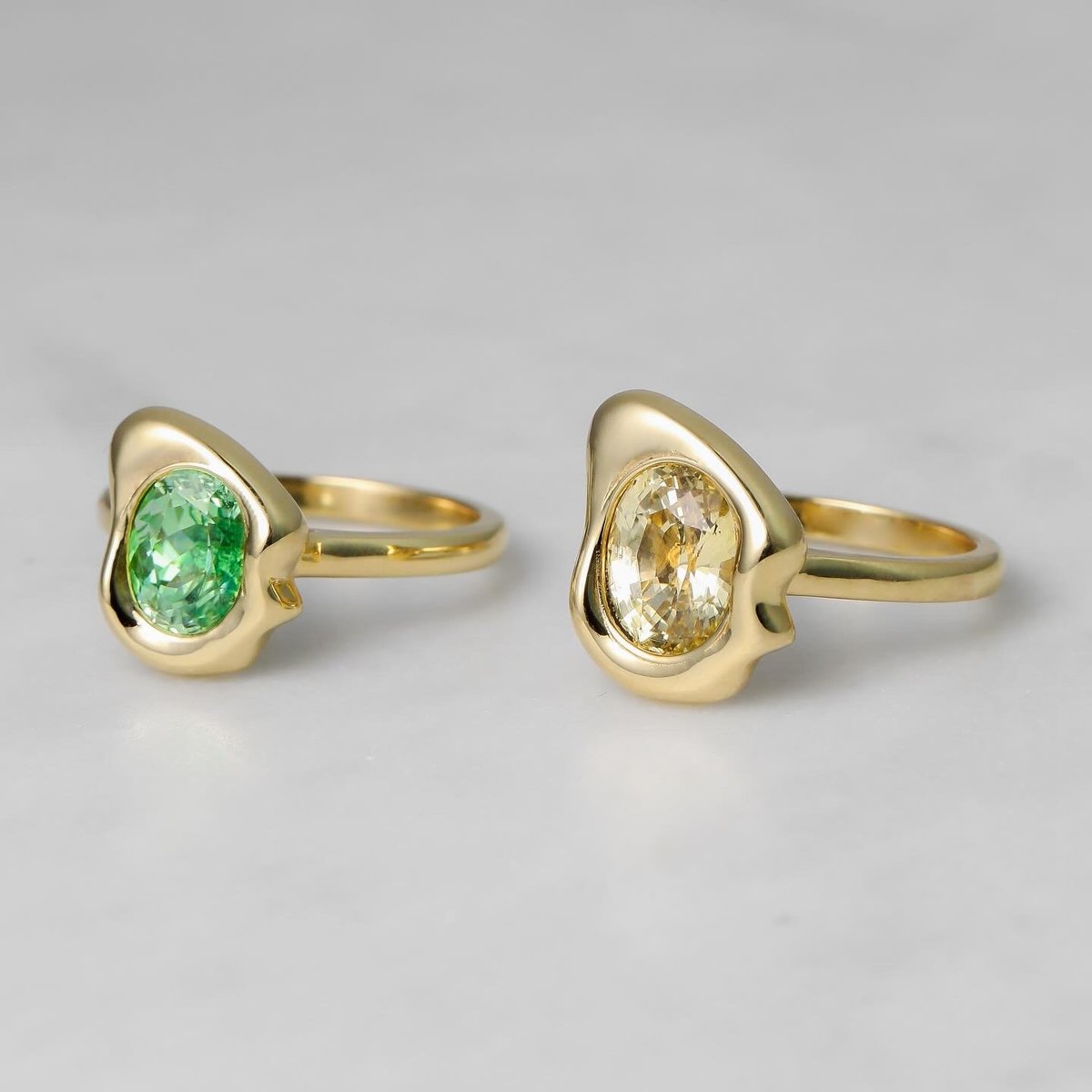 Two custom yellow gold rings with organic bezels holding green and yellow stones