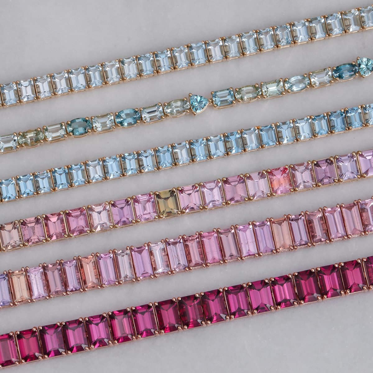 Rows of custom gemstone tennis bracelets in graduated blues and pinks